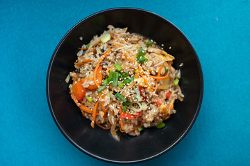 Plate with asian food, rice with vegetables and sesame, blue background