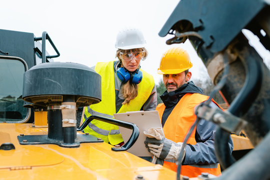 Frau und Mann als Arbeiter im Steinbruch auf einem Bagger