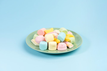 Green plate with marshmallow isolated on blue background.