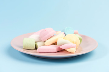 Pink plate with marshmallow isolated on blue background.