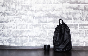 Black backpack and cup on the floor over background of grey brick