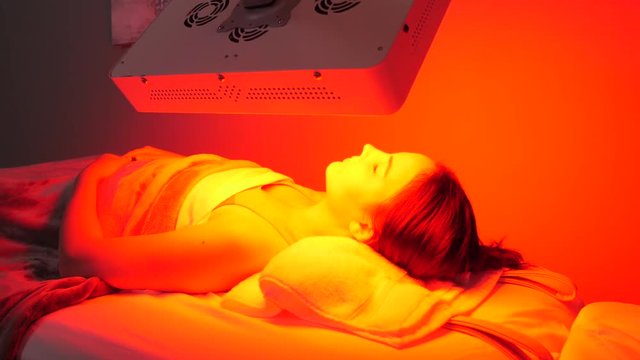Camera pans left to right as patient lies on back under infrared lamp that is aimed at her face