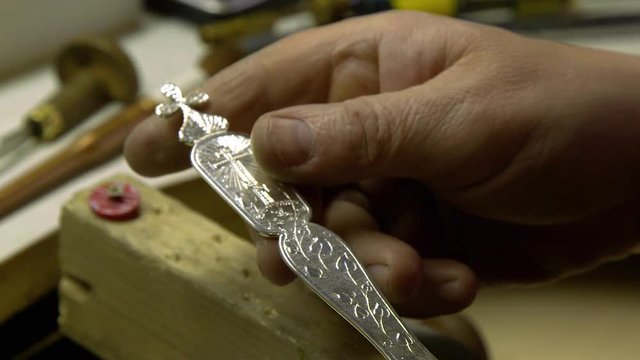 jeweler in the workshop engraves a silver spoon with beautiful painted patterns