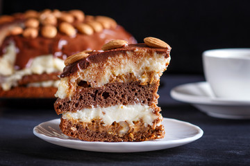 Homemade chocolate cake with milk cream, caramel and almonds on black wooden background.