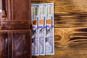 Brown leather wallet and one hundred dollar banknotes on the wooden background. Top view