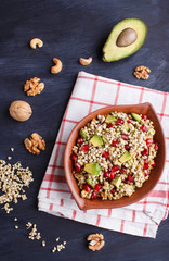 Salad of germinated buckwheat, avocado, walnut and pomegranate seeds in clay plate on black wooden background.