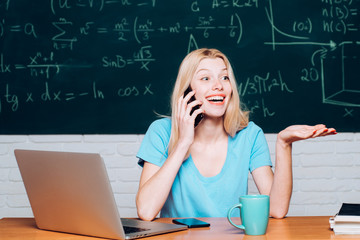 Student girl with happy face expression near desk with school supplies. Happy mood smiling broadly in university. Student working on laptop in college