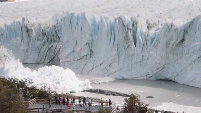 Tourists watching a chunk of glacier collapsing into the lake Argentino on the Patagonia region. Slow motion.
