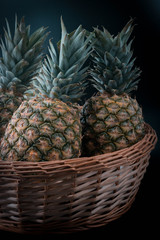 three pineapples in a wicker basket on an isolated black background