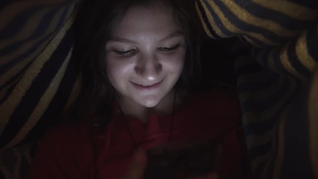 Caucasian girl underneath the covers messaging on cellphone and smiling