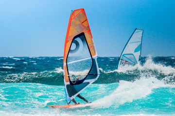 water sports: windsurfers riding waves with colored sails in oceanic blue water
