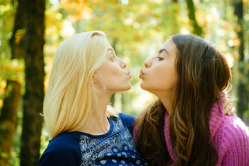 Fototapeta premium Friendly kiss. Glad to see you. Girls friends kissing. Girlish friendship concept. Blonde and brunette walking in autumn park defocused background. Women kiss cute faces close up. Come on kiss me