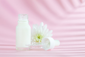 Natural cosmetics: serum with dropper and white flower on pink background with shadow.