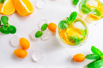 Summer citrus drink with orange, kumquat, mint and ice cubes on white background. Flat-lay, top view.