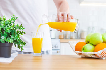 Man pouring orange juice from jug into glass in the kitchen.
