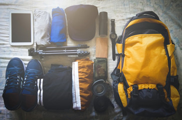 Travel concept of traveler with yellow backpack, tablet, t-shirt, hat, wallet, watch, shoes, belt, shorts, perfume, power bank, camera tripod. Planning trip in summer. Top view. selective focus
