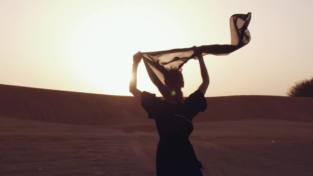 A woman with a black scarf in her hands in sand dunes in a Desert