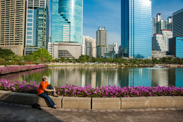 tourist girl in bright shirt sitting near blue lake in park in Bangkok, traveler resting near big lake and watching for reflections of skyscrapers - 268938432