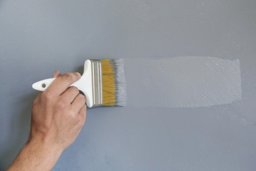 Man painting with a paintbrush over a grey wall