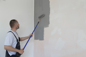 Man painting with gray paint over a white wall