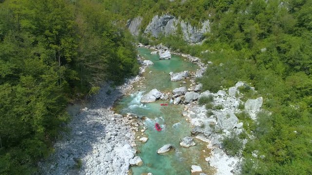 AERIAL: Unrecognizable tourists on a kayaking and rafting trip float around the emerald river. Flying above whitewater rapids of Soca river and towards active tourists rafting in the summertime.