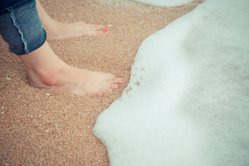 Female feet with red pedicure wear blue jean stand on the beach sand