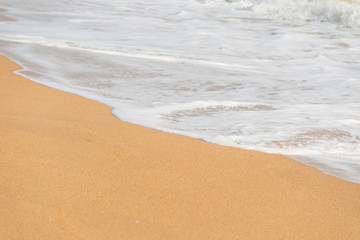 Fototapeta na wymiar Soft foam wave and sea on the sandy beach