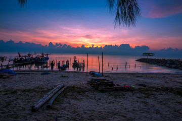 Obraz premium The blurred background of the morning twilight by the sea, changing the color of the beautiful sky, there is a fishing boat docked waiting to go out to find fish again.