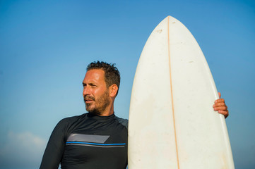 handsome and attractive surfer man in neoprene swimsuit holding surf board posing cool after surfing enjoying Summer water sport and holidays