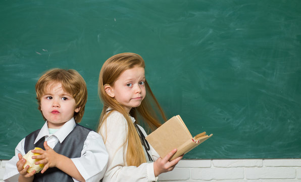 Funny little boy and cute little girl pointing up on blackboard. Copy space. Blackboard background. School kids. Kids from primary school. First school day.