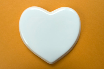 White glossy porcelain heart on a dark yellow background. Wedding card; A love note. Copy space