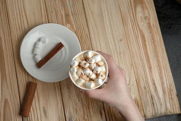 Hands holding a mug of hot chocolate or coffee with marshmallows on a dark rustic wooden table. Christmas and New year background. Top view