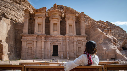 Asian woman tourist in white dress sitting and looking at Ad Deir or El Deir, the monument carved...