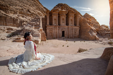 Asian woman tourist in white dress sitting at Ad Deir or El Deir, the monument carved out of rock...