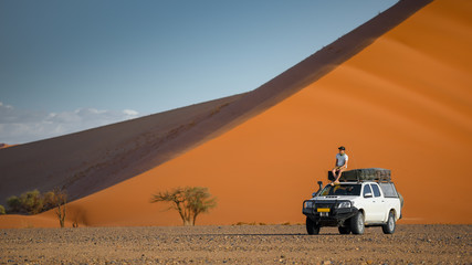 Young Asian man tourist sitting on camper car near orange sand dune landscape. Travel desert in...