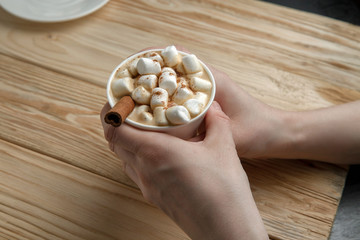 Hands holding a mug of hot chocolate or coffee with marshmallows on a dark rustic wooden table. Christmas and New year background. Top view