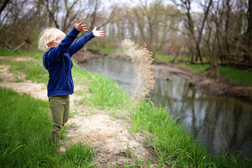 Little Child Playing Outside by the River, Throwing Sand in the Water