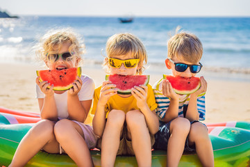 Children eat watermelon on the beach in sunglasses