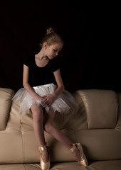 little ballerina in pointe sits and resting on the sofa. cute ballerina in the dance class is studying ballet. Classical dance, ballet