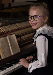 strict little girl in a big glasses playing the piano, child imitates teacher