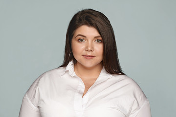 Portrait of charming plus size young woman dressed in formal wear posing in studio. Isolated image...