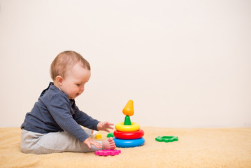 Cute baby playing with colorful toy pyramid in light bedroom. Toys for little kids. Child with educational toy. background with copy space