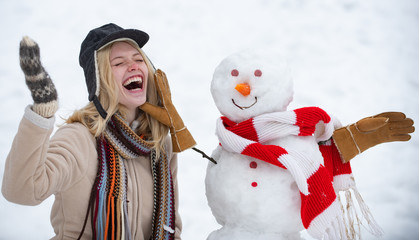 Winter love concept. Happy girl plaing with a snowman on a snowy winter walk. Making snowman and...