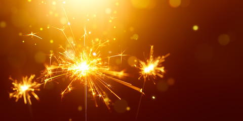 Fototapeta na wymiar Glittering burning sparkler against golden bokeh background