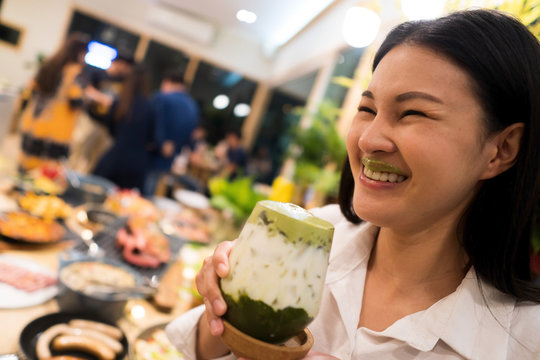 Beautiful Adult working woman drink Ice Milky Green Tea and smile with foam on her lips  atmosphere with many food plates and people in restaurant, selective focus blur