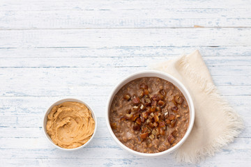 Delicious oatmeal in a white bowl, dates fruits and cocoa. healthy breakfast on light blue background