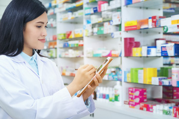 Pharmacist working with a tablet computer in the pharmacy holding it in her hand while reading...