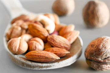Almonds, Hazelnuts, Walnuts, Cashew Nuts in a Wooden Spoon, and Three Whole Walnuts on Gray Background. Healthy Organic Snack, Breakfast. Color Pop Effect.