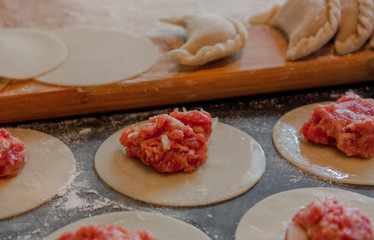 The process of making dumplings with minced meat on a wooden table in closeup. In the background are finished products. Selective focus.