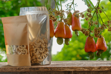 Cashew nuts in the packaging bag with floor wooden and red ripe fruit background on the tree